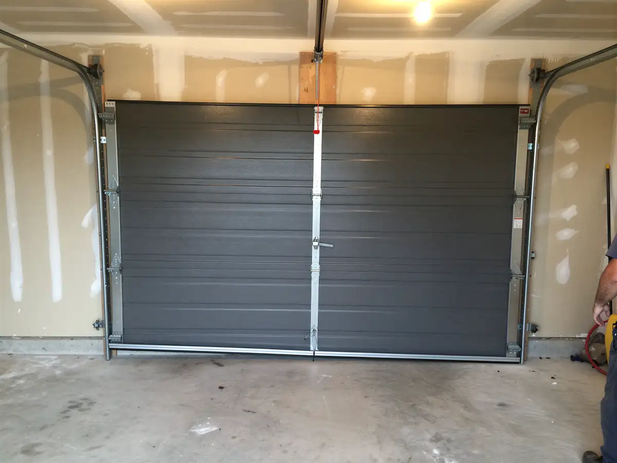 A new gray garage door is installed in an unfinished garage.
